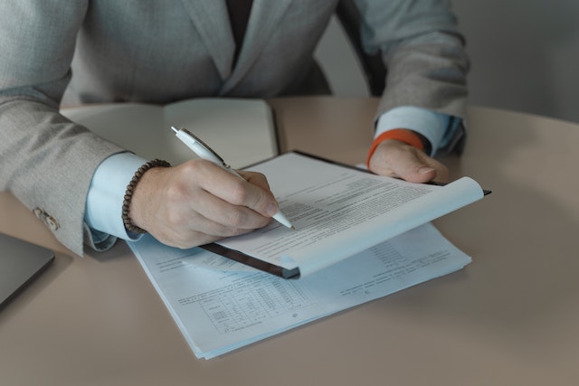 person in a gray suit looking over a document on a clipboard and make notes with a pen
